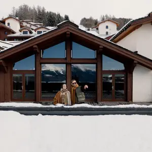 casal em frente a uma varanda com telhado coberto de neve observando a paisagem