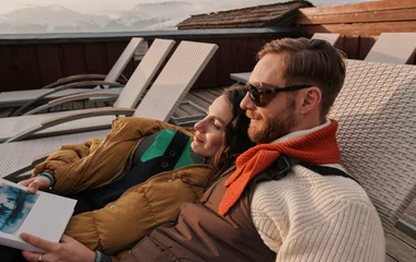 Casal deitado em cadeira, lendo um livro