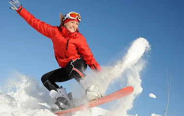 Mulher sorrindo enquanto salta no snowboard.