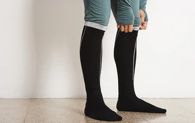 Pessoa ajustando uma meia preta de cano alto.