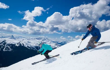Duas pessoas esquiando em dia de sol.