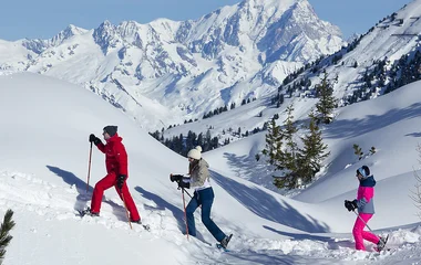 Três pessoas caminhando com raquetes na neve.