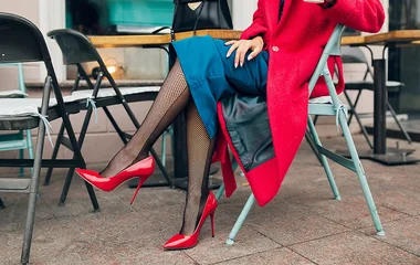 Mulher sentada com meia calça e casaco vermelho.