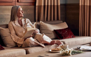 Mulher sentada no sofá lendo um livro e tomando café