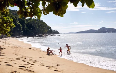 pai, mãe e filha brincando em praia paradisíaca
