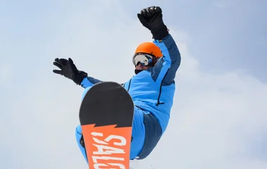 Homem saltando durante a prática de snowboard.