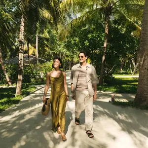 Casal andando de mãos dadas em uma área arborizada no resort.