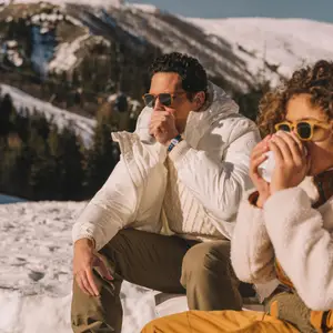 Casal bebendo chocolate quente em uma xícara olhando paisagem de neve.