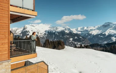 mulher em sacada de chalé em meio as montanhas nevadas