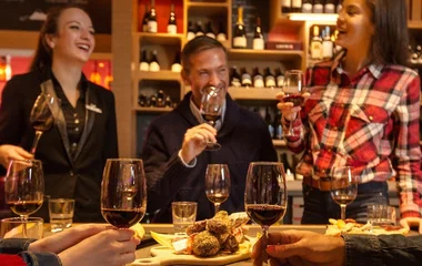 Cinco pessoas se divertindo enquanto bebem vinhos numa adega.