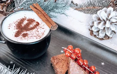 Xícara de chocolate quente com canela em pau na borda, ao lado de dois pedaços de brownie.