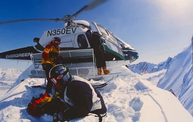 Três pessoas perto de um helicóptero prestes a praticar heli skiing.