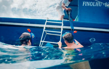 Two guests in the water's ocean about to climb on a blue boat
