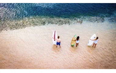 Group of three people standing on the beach holding surfboards at the beach shore