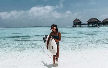 Frau hält ein Surfboard am Strand auf den Malediven
