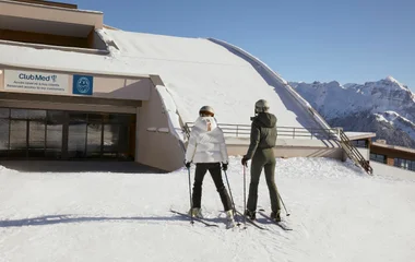 Dos mujeres con ropas e equipos de esquí en dirección al resort.