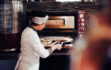 Mujer mirando a las pizzas en el horno.