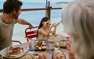 Mãe em pé e filho e filha tomando sorvete durante almoço vcom vista para o mar