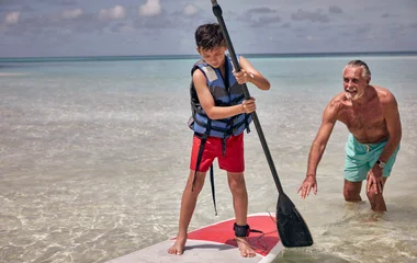 KInd steht auf dem Surfbrett mit einem Paddel