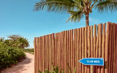 Placa na praia escrita "Club Med" mandando seguir para uma direção.
