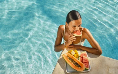 Femme au bord d'une piscine dégustant des fruits exotiques