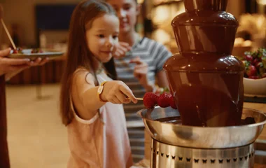 Criança aproveitando cascata de chocolate com palitinho de morango.