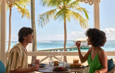 Casal comendo no restaurante com a praia ao fundo.