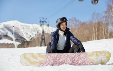 Mulher sentada na neve depois de praticar snowboard.