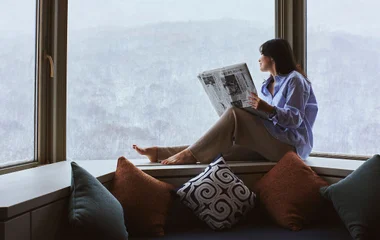 Woman reading by the window looking at the snow
