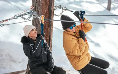Duas pessoas descendo de tirolesa numa paisagem de neve.